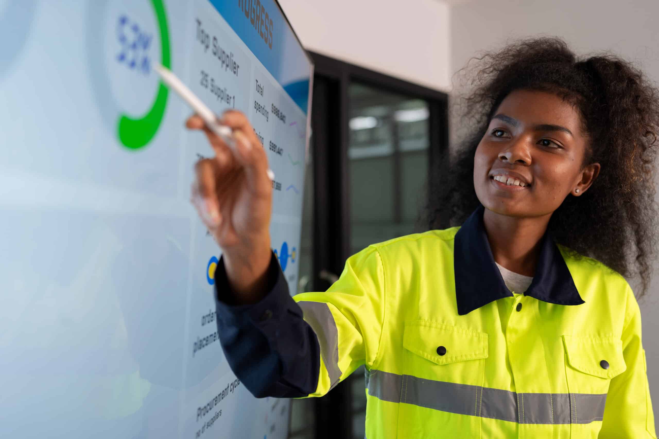 Woman in high-visibility jacket points at a data chart during manufacturing analytics consulting.