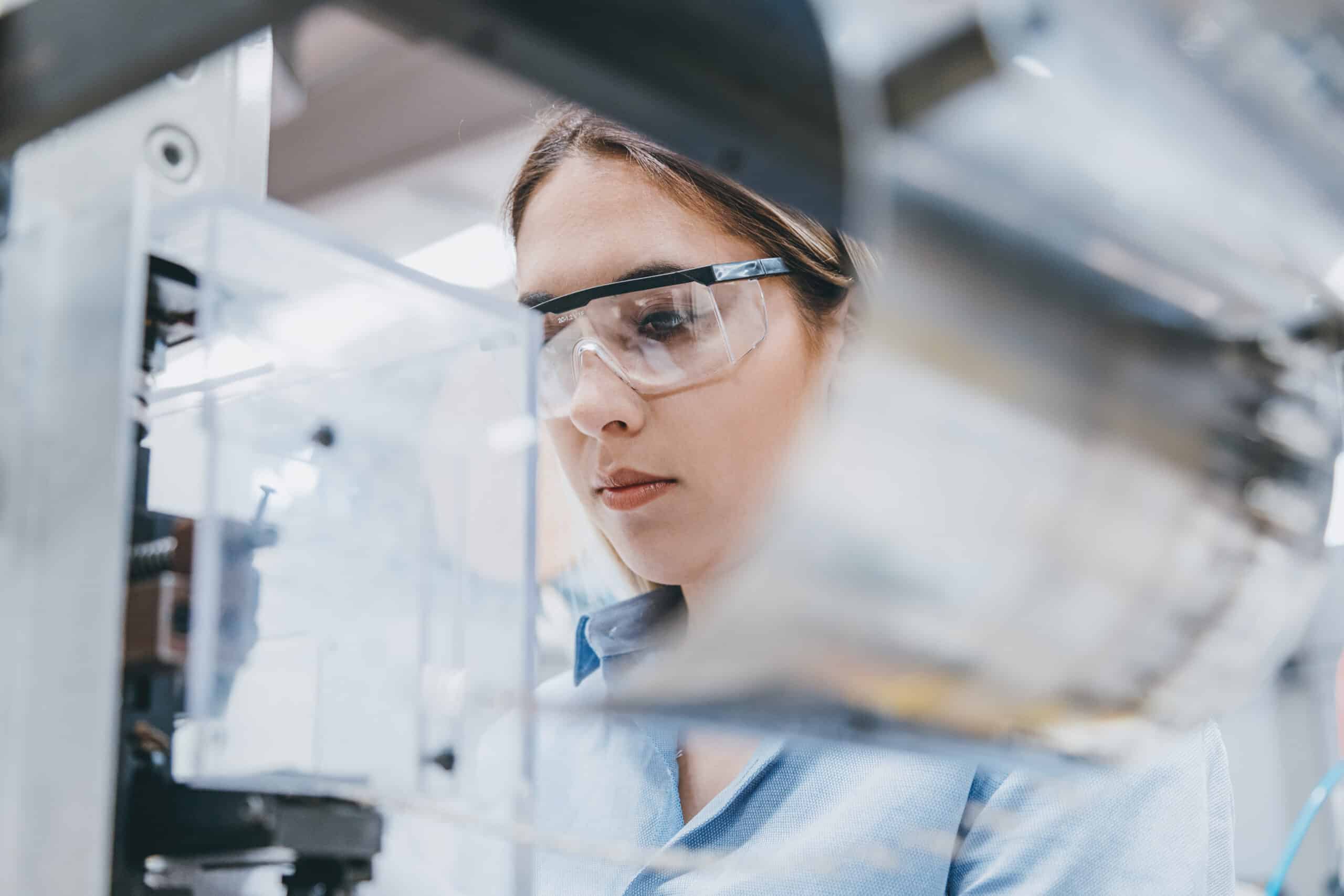 Woman wearing safety goggles operates machinery, guided by manufacturing engineering consultants.