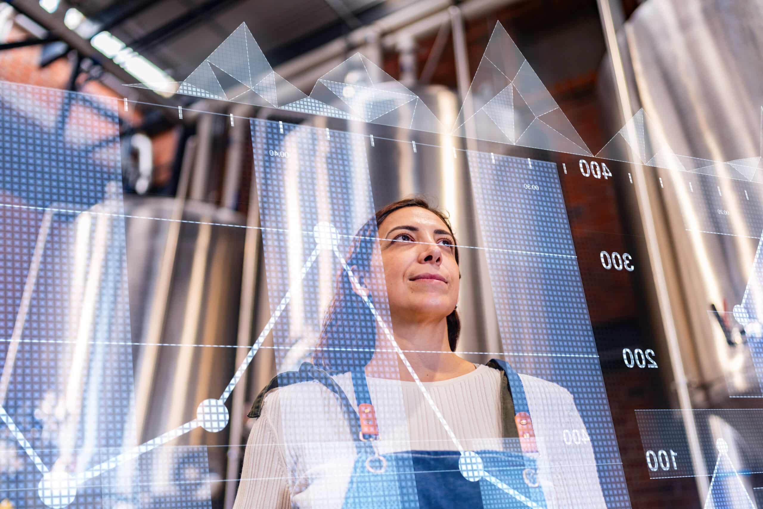 Woman in factory looking up, overlaid with financial charts and manufacturing execution system data.