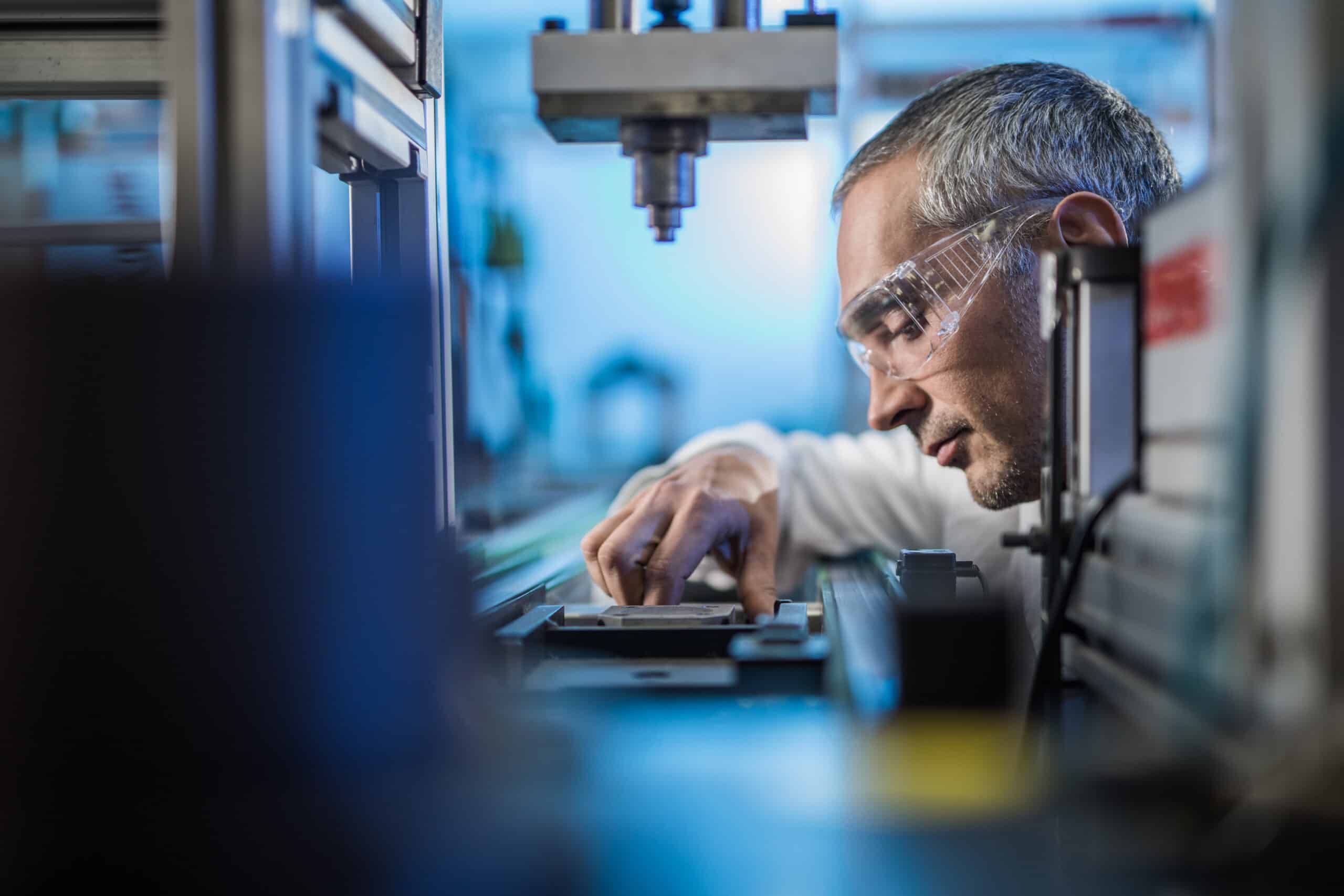 Man wearing safety glasses working with machinery in a Manufacturing Quality Consulting lab.