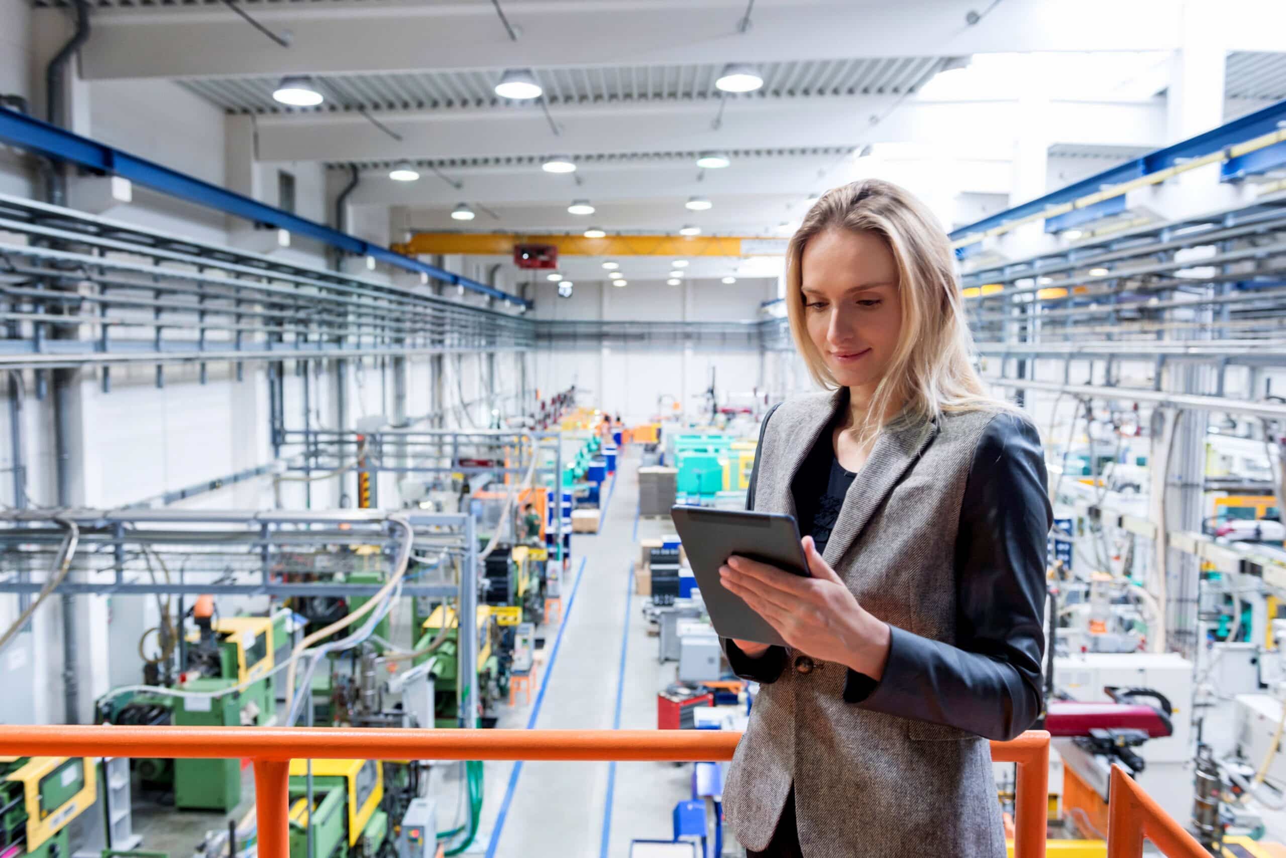 Woman using tablet in modern factory, overseeing machinery and plm consulting processes.