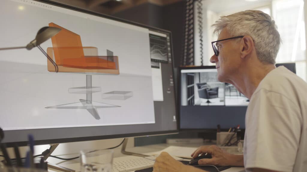 Person designing an orange chair on a computer, showcasing Product Design Consulting expertise.
