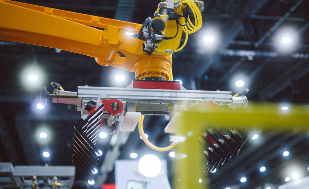 Yellow robotic arm operates in a modern, brightly lit factory with sustainable manufacturing consulting.