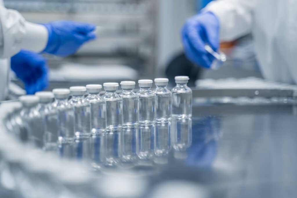 Gloved hands near vials on a metal surface, representing Life Sciences Market Access in a lab.