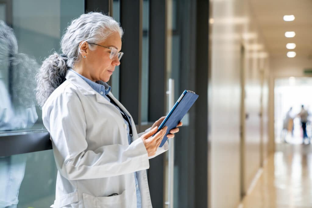 Older female doctor reads a tablet, exploring AI Pilots to improve healthcare performance.