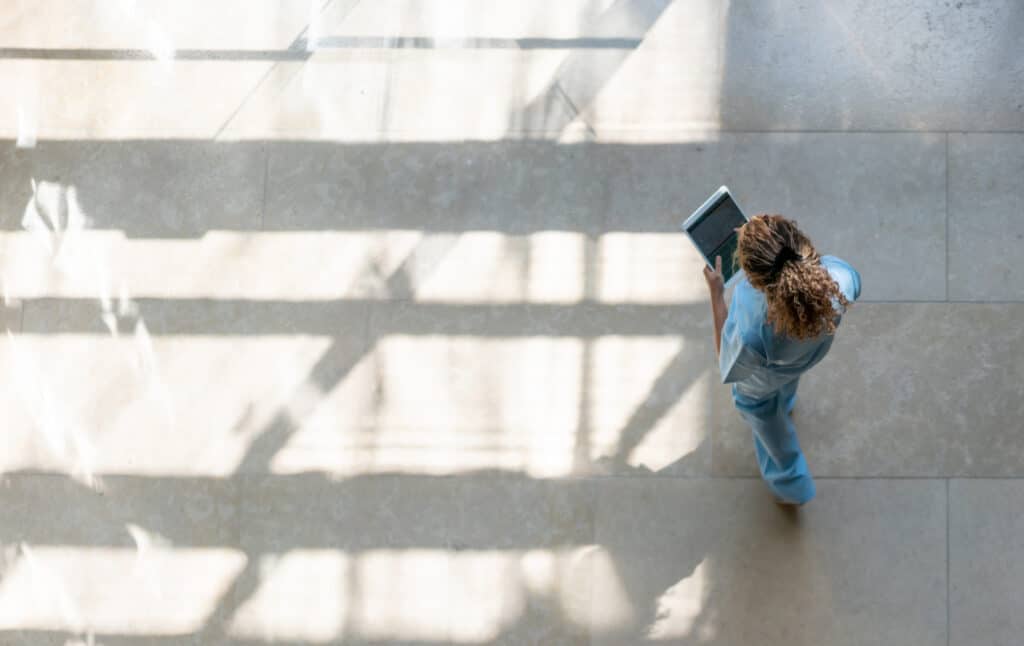Person in scrubs walks indoors holding a tablet, reflecting digital health adoption trends.