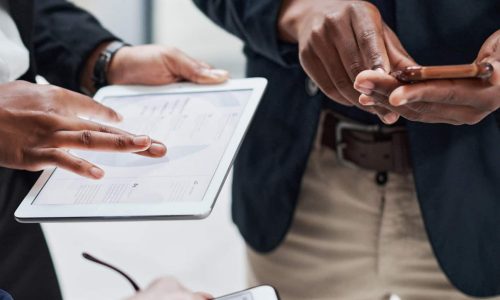 Three people using a tablet and smartphones in a Risk Management Consulting setting.