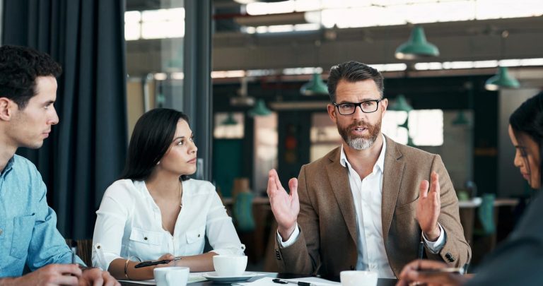 iStock-1434124353123 Five people at a table in a business meeting discussing talent acquisition consulting.